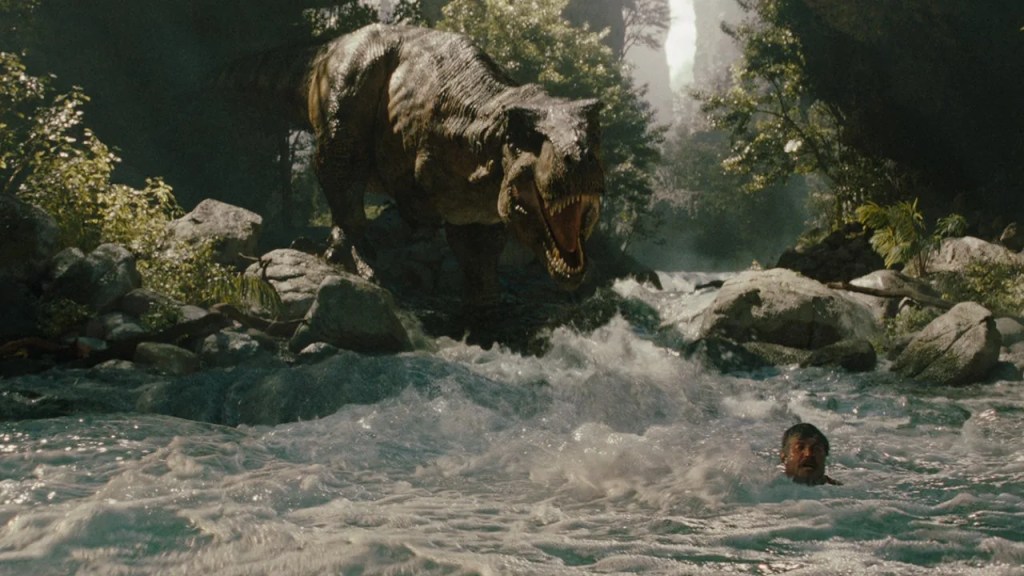 Dramatic still from the Jurassic World Rebirth trailer showing a Tyrannosaurus Rex roaring over a person in a turbulent river, hinting at the adapted river raft scene.