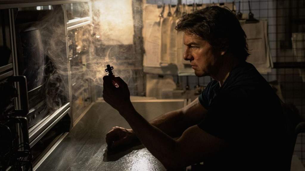 Tom Cruise as Ethan Hunt in M:I: Final Reckoning, intently examining a small, crucial cross-shaped key in a dimly lit workshop.