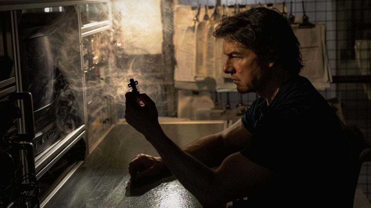 Tom Cruise as Ethan Hunt in M:I: Final Reckoning, intently examining a small, crucial cross-shaped key in a dimly lit workshop.