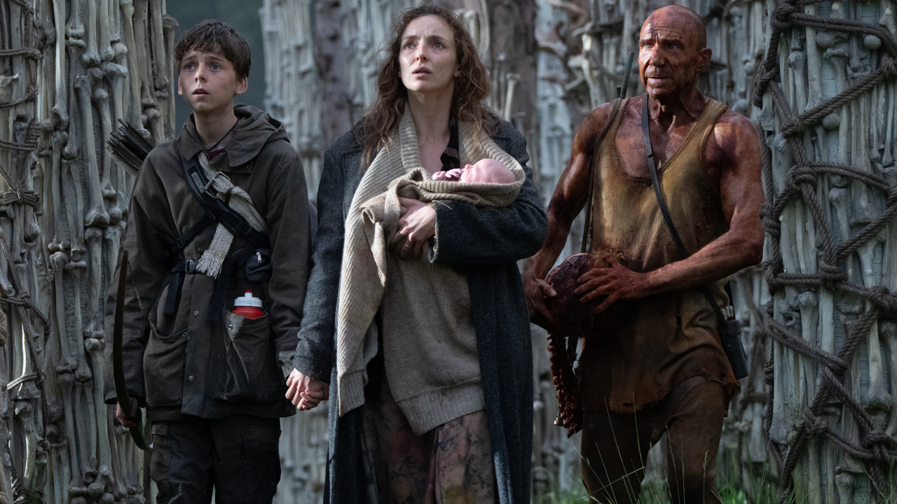 Characters in 28 Years Later walk through a bone structure while holding a baby.