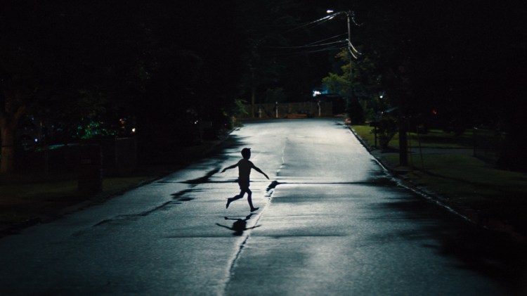 The silhouette of a lone child runs across a deserted suburban street at night in a scene from the horror mystery Weapons.